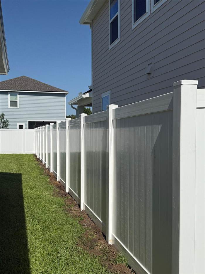 Close view of a white vinyl privacy fence along a side yard