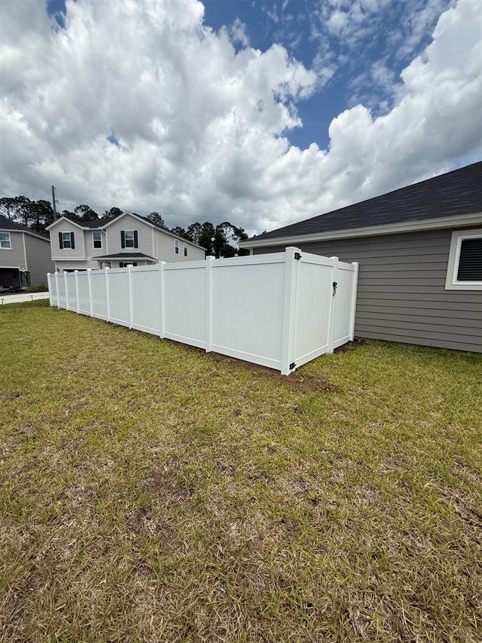 White vinyl privacy fence enclosing a yard, ending at a gate